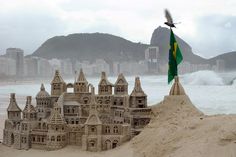 a sand castle on the beach with a flag flying over it and buildings in the background