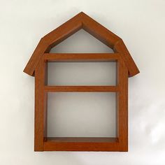 a wooden shelf with a small house on it's top and bottom section, against a white wall