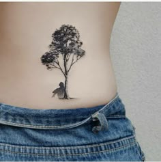 a woman's stomach with a small tattoo of a tree and a man sitting under it