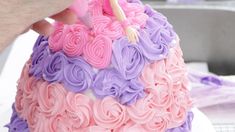 someone is decorating a cake with pink, purple and lavender frosting on it