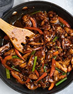 a skillet filled with meat and vegetables being stirred by a wooden spoon on the side