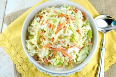 a white bowl filled with coleslaw on top of a yellow napkin next to a spoon