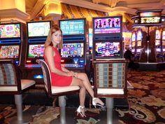 a woman in a red dress sitting on a chair next to slot machines