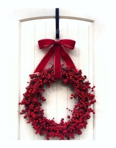 a red wreath hanging on the side of a white door with a bow around it