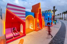 a woman is riding her bike past brightly colored houses on the street in front of palm trees