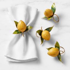 three napkin rings with yellow flowers and leaves on them sitting next to a white cloth