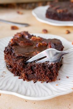 a piece of chocolate cake on a white plate with a fork in it and someone holding a knife