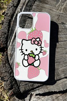 a hello kitty phone case sitting on top of a piece of tree trunk with strawberries