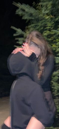 a woman is sitting on the ground in front of some trees with her hands covering her face