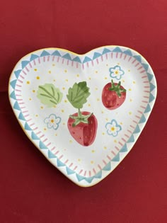 a heart shaped plate with strawberries painted on the front and sides, sitting on a red surface