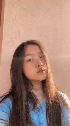 a woman with long brown hair standing next to a wall and looking at the camera