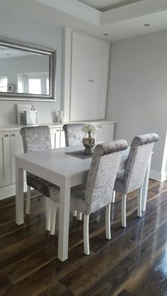 a dining room table with four chairs and a mirror on the wall above it, in front of white cabinets