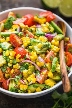 a salad with corn, tomatoes, cucumbers and onions in a white bowl