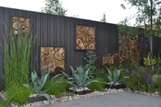 an outdoor garden with rocks, plants and wood slices on the side of a building