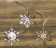 three metal snowflakes hanging from strings on a wooden surface