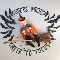 a baby sitting on top of a broom in front of a sign with bats and pumpkins