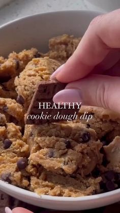 someone is holding a cookie dough tip in a bowl full of cookies and chocolate chips