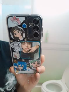 someone is holding up their cell phone case with pictures of people on it in front of a toilet