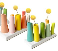 several different colored vases with flowers in them sitting on a white surface, side by side