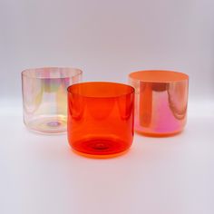 three different colored glass vases sitting next to each other on a white table top