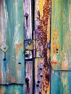 an old rusty door is painted green and blue with rust on the paint peeling from it