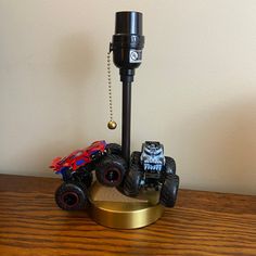 two toy trucks on top of a wooden table next to a metal object with chains hanging from it's sides