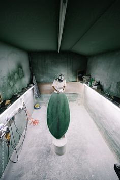 a man sitting on top of a green surfboard in a room filled with other items