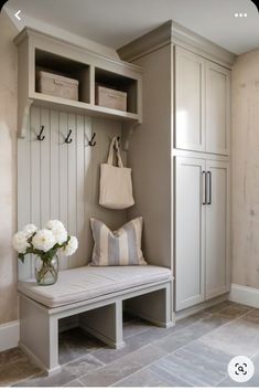 a white bench sitting next to a wall with baskets on top of it and a vase filled with flowers