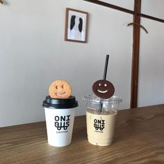 two coffee cups with smiley faces and one cup has a cookie on top, while the other is empty