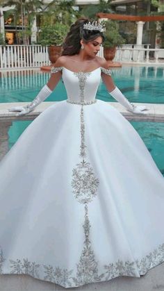 a woman in a white wedding dress standing next to a pool wearing a tiara