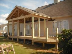 a wooden porch sitting on top of a lush green field next to a building with white windows