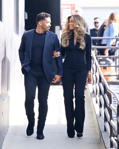 a man and woman are walking down the sidewalk holding hands while wearing all black outfits