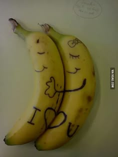 two bananas with faces drawn on them sitting next to each other in front of a white wall