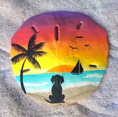 a painted rock with a dog and sailboat in the ocean at sunset on a sandy beach