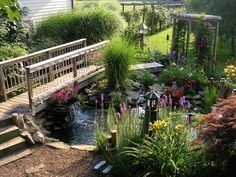 a bridge over a small stream in a garden with lots of flowers and plants around it