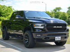 a black ram truck is parked in a parking lot with trees and bushes behind it