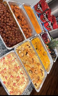 several trays of food are lined up on a counter top in front of candy bars