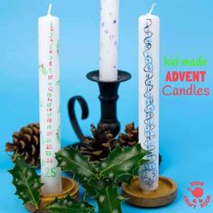 three candles with writing on them sitting next to holly leaves and pine cones in front of a blue background