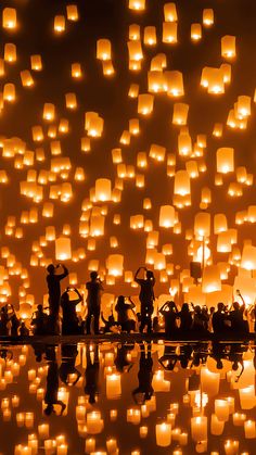 many people are flying lanterns in the sky with water reflecting on the ground and one person is taking pictures