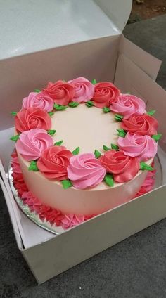 a cake in a box with pink flowers on top and green leaves around the edges