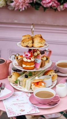 a pink table topped with three tiered trays filled with pastries and drinks