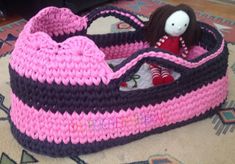 a crocheted pink and black purse with a doll in it on the floor