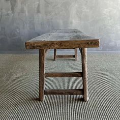 a wooden table sitting on top of a carpeted floor next to a gray wall