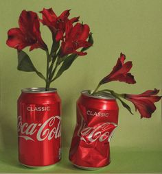 two cans with red flowers in them on a green surface next to each other, one has the word coca - cola written on it