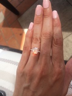 a woman's hand holding an engagement ring with a diamond in the middle and pink manicured nails