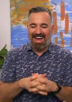 a man standing in front of a painting with his hands folded and smiling at the camera