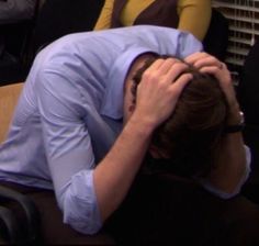 a man is covering his face with his hands while sitting in front of a woman