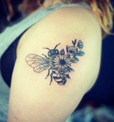 a woman's shoulder with a bee and flowers tattoo on the back of her arm