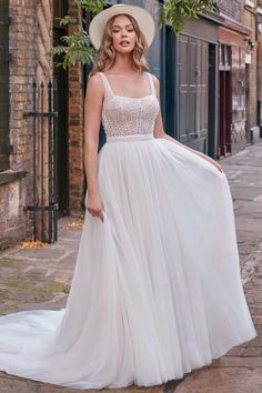 a woman wearing a white dress and hat standing on the sidewalk in front of brick buildings