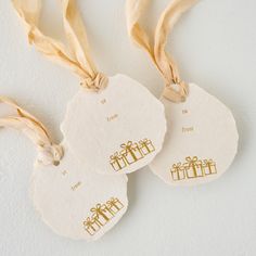 three white tags with gold foiled gifts hanging from them on a string against a white wall